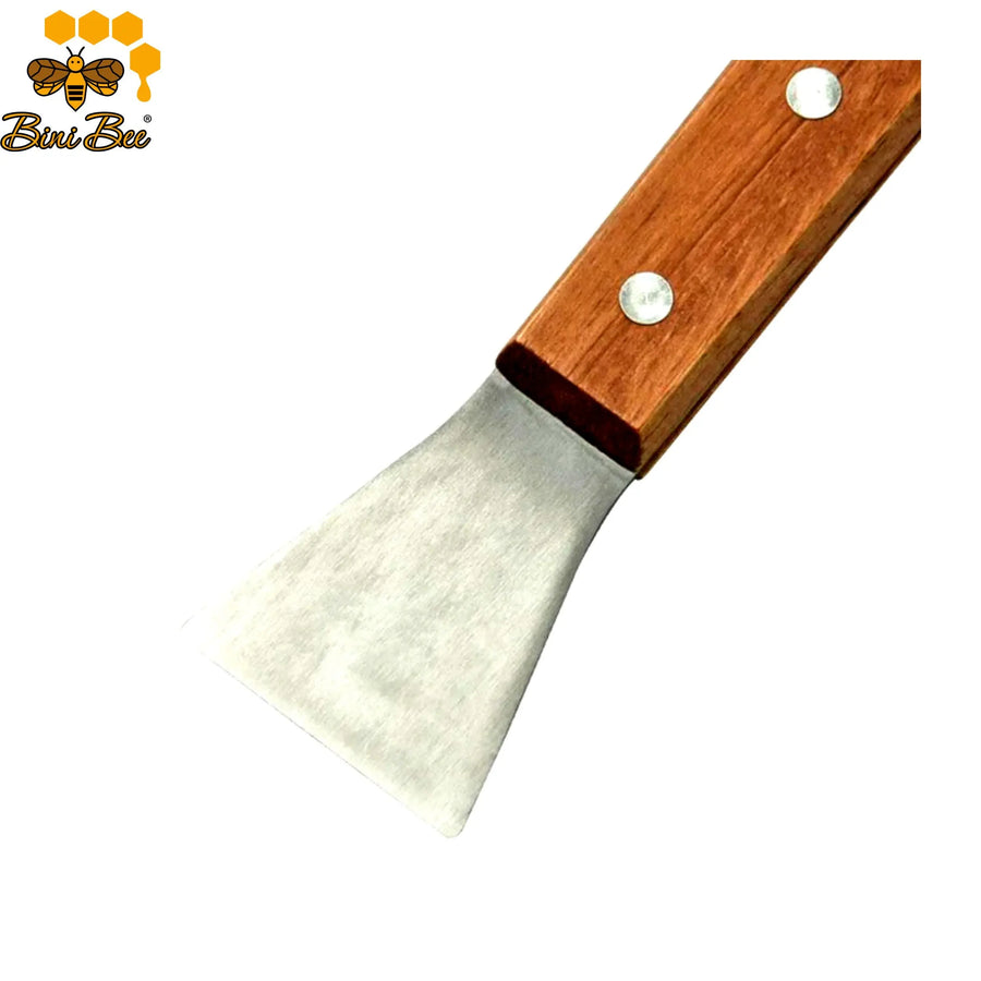 Handheld stainless steel hive scraper with a smooth wooden handle being used to clean propolis off a wooden Langstroth beehive box